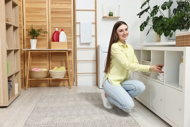 Photo of Beautiful young woman taking towels from drawer in laundry room