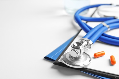 Stethoscope, clipboard and pills on light background, closeup. Medical equipment