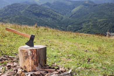 Tree stump with axe in mountains, space for text