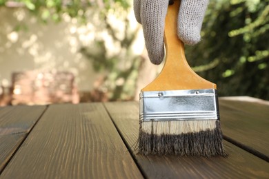 Photo of Man applying wood stain onto wooden surface outdoors, closeup. Space for text