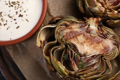 Tasty grilled artichoke and sauce on table, top view