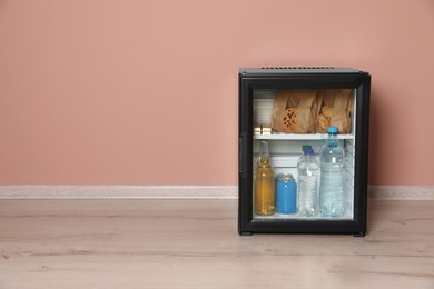 Photo of Mini bar filled with food and drinks near pale pink wall indoors, space for text