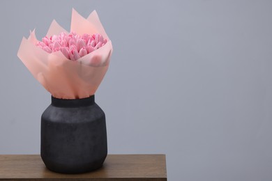 Photo of Bouquet of beautiful pink tulips in vase on wooden table against light grey background, space for text