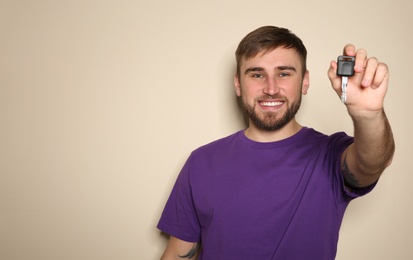 Photo of Happy young man with car key on color background, space for text. Getting driving license