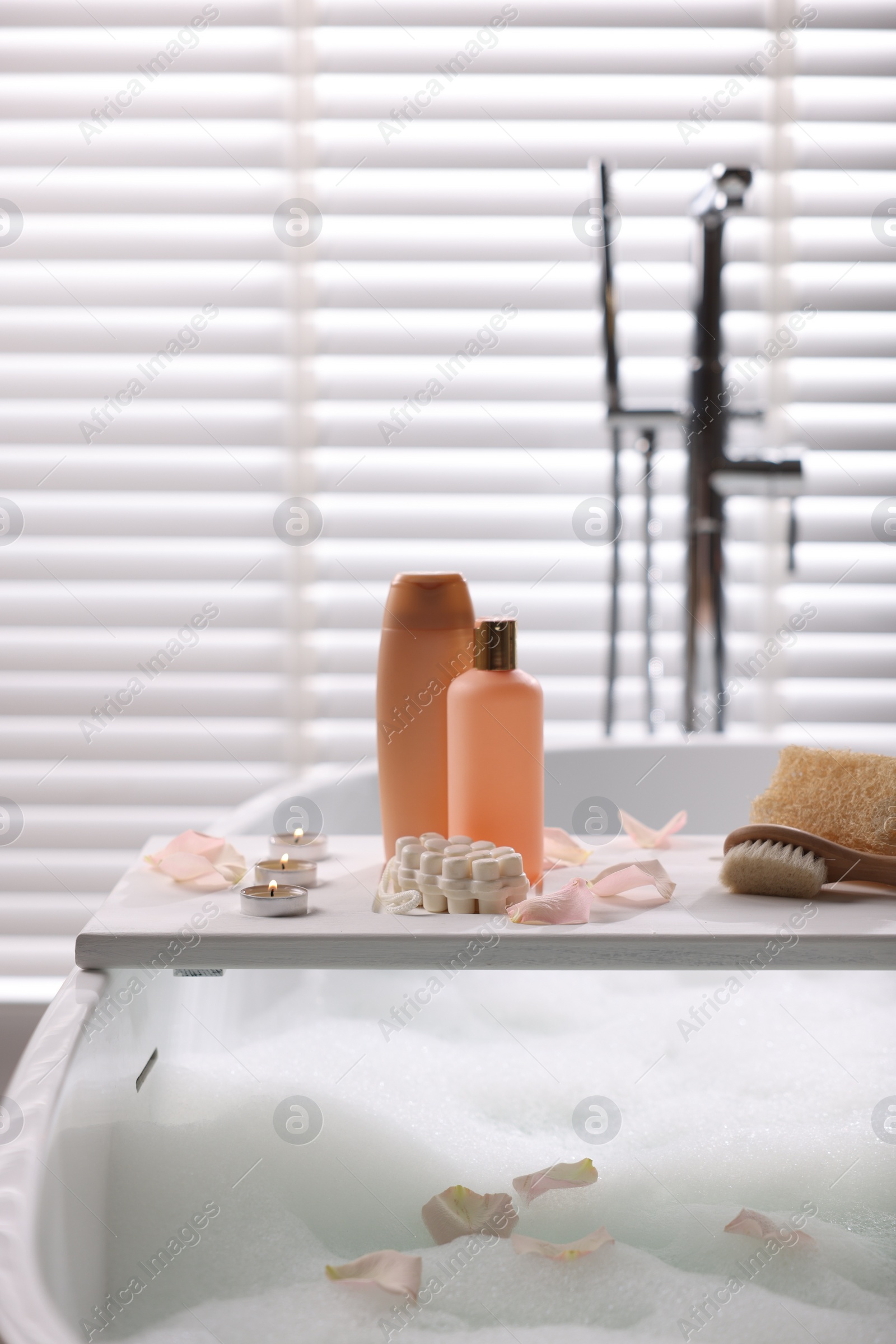 Photo of Wooden tray with toiletries and flower petals on bathtub in bathroom