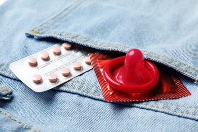 Photo of Red condom and birth control pills in pocket of jeans, closeup. Safe sex concept
