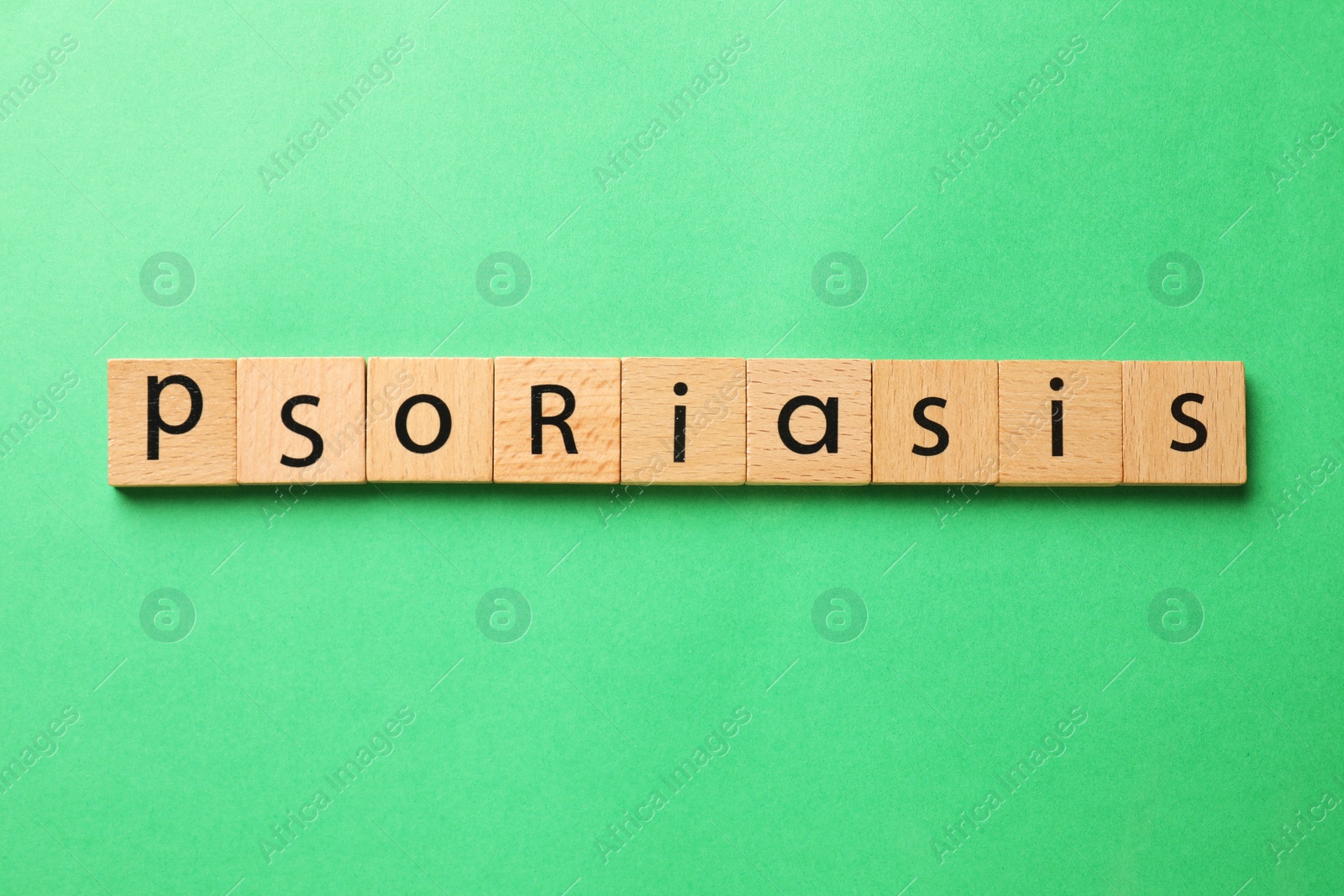 Photo of Word Psoriasis made of wooden squares with letters on green background, top view