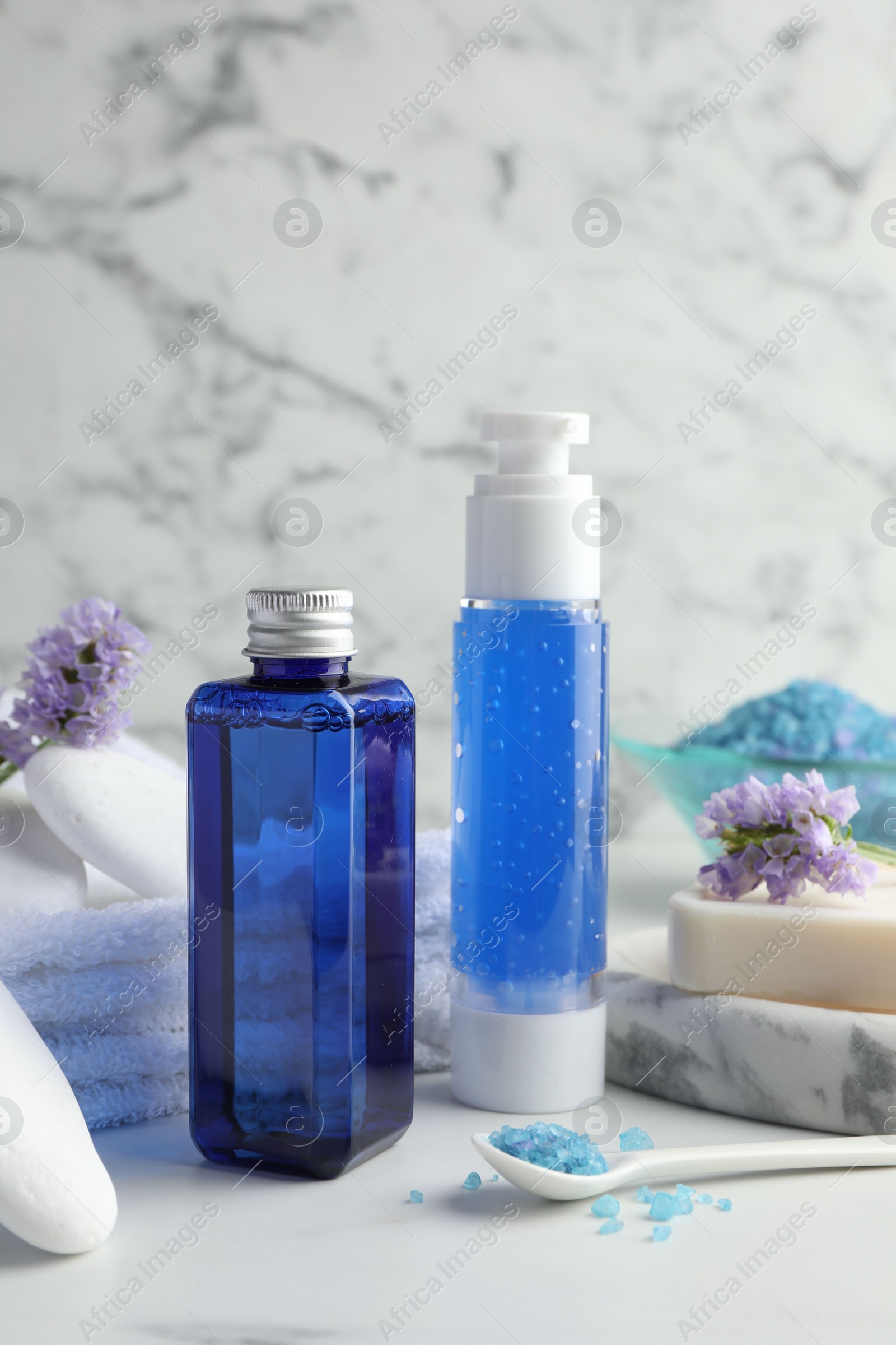 Photo of Spa composition. Bottles of cosmetic products, sea salt, stones, soap and flowers on white table