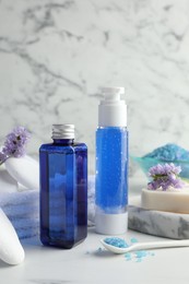 Photo of Spa composition. Bottles of cosmetic products, sea salt, stones, soap and flowers on white table