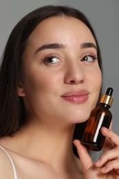 Beautiful young woman with essential oil on light grey background, closeup