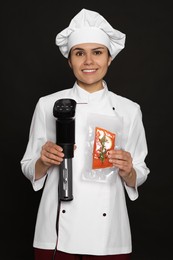 Photo of Chef holding sous vide cooker and salmon in vacuum pack on black background