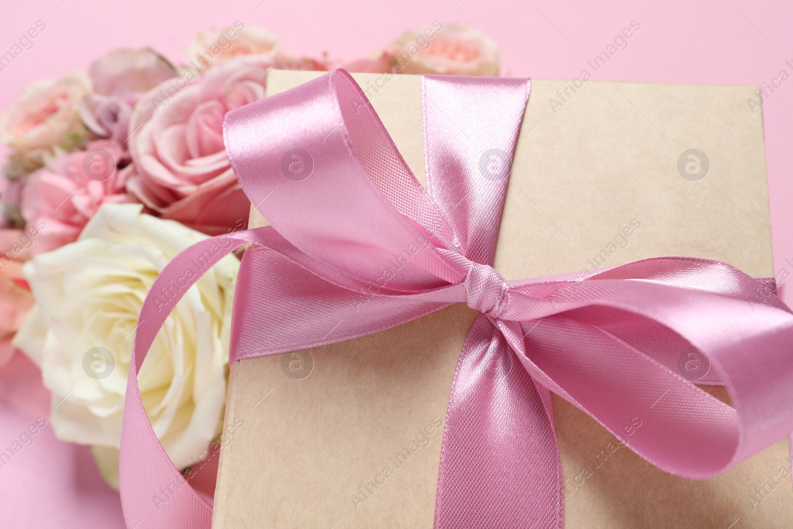 Photo of Gift box and beautiful flowers on pink background, closeup