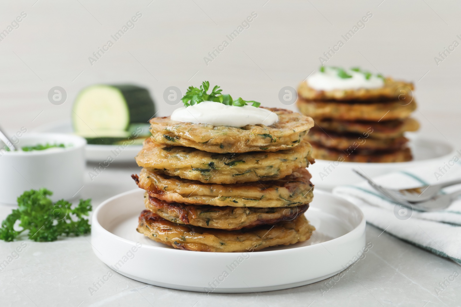 Photo of Delicious zucchini pancakes with sour cream served on light grey table