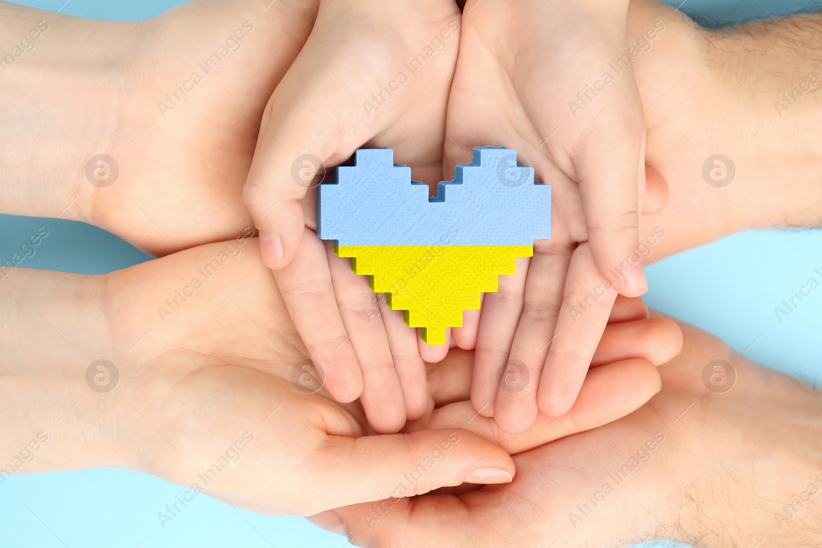 Image of Stop war in Ukraine. Family holding heart shaped toy with colors of Ukrainian flag in hands on light blue background, closeup