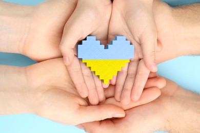 Stop war in Ukraine. Family holding heart shaped toy with colors of Ukrainian flag in hands on light blue background, closeup