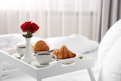 Photo of Tray with tasty breakfast and flowers on bed at home, space for text