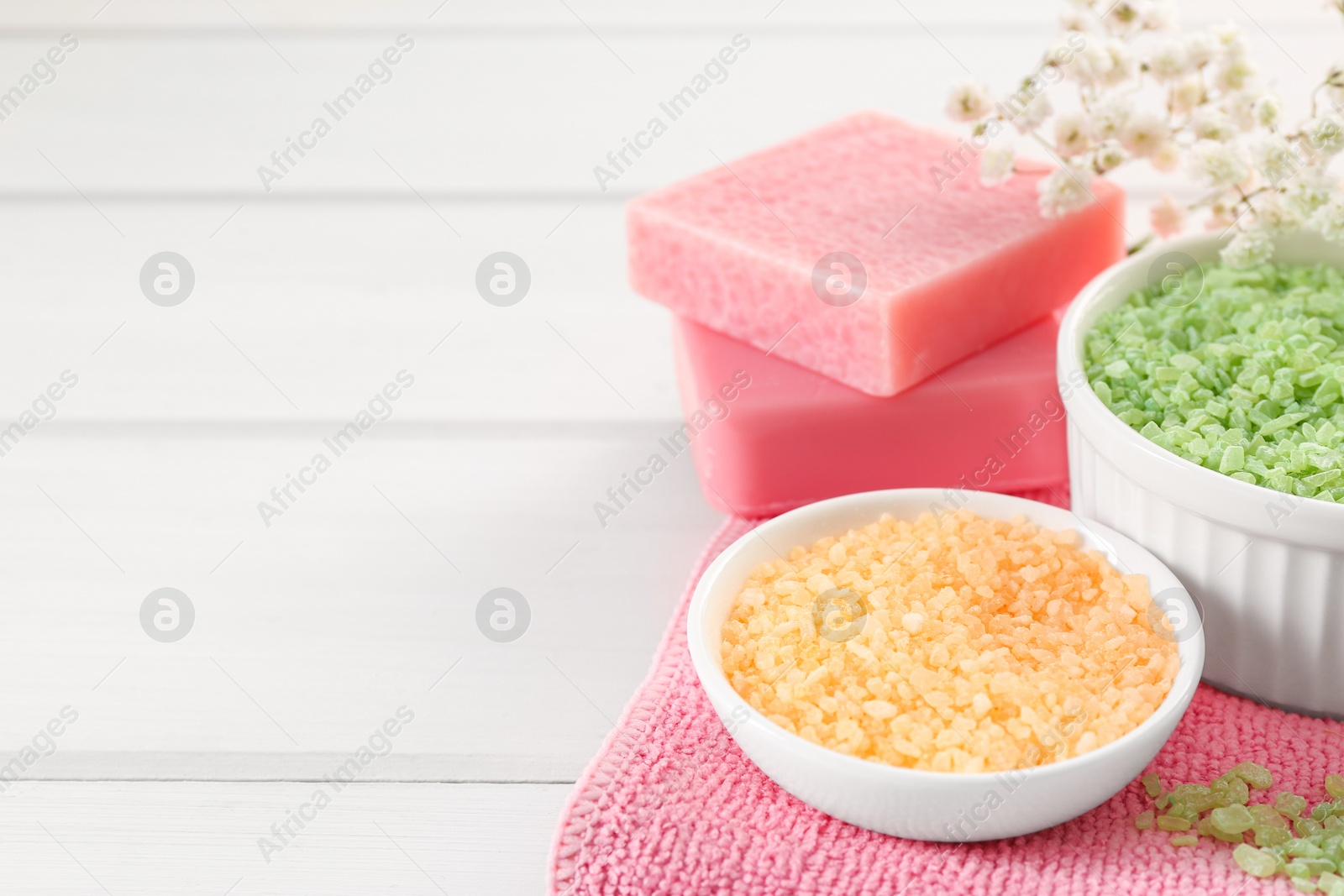 Photo of Bowls with sea salt and soap bars on white wooden table. Space for text