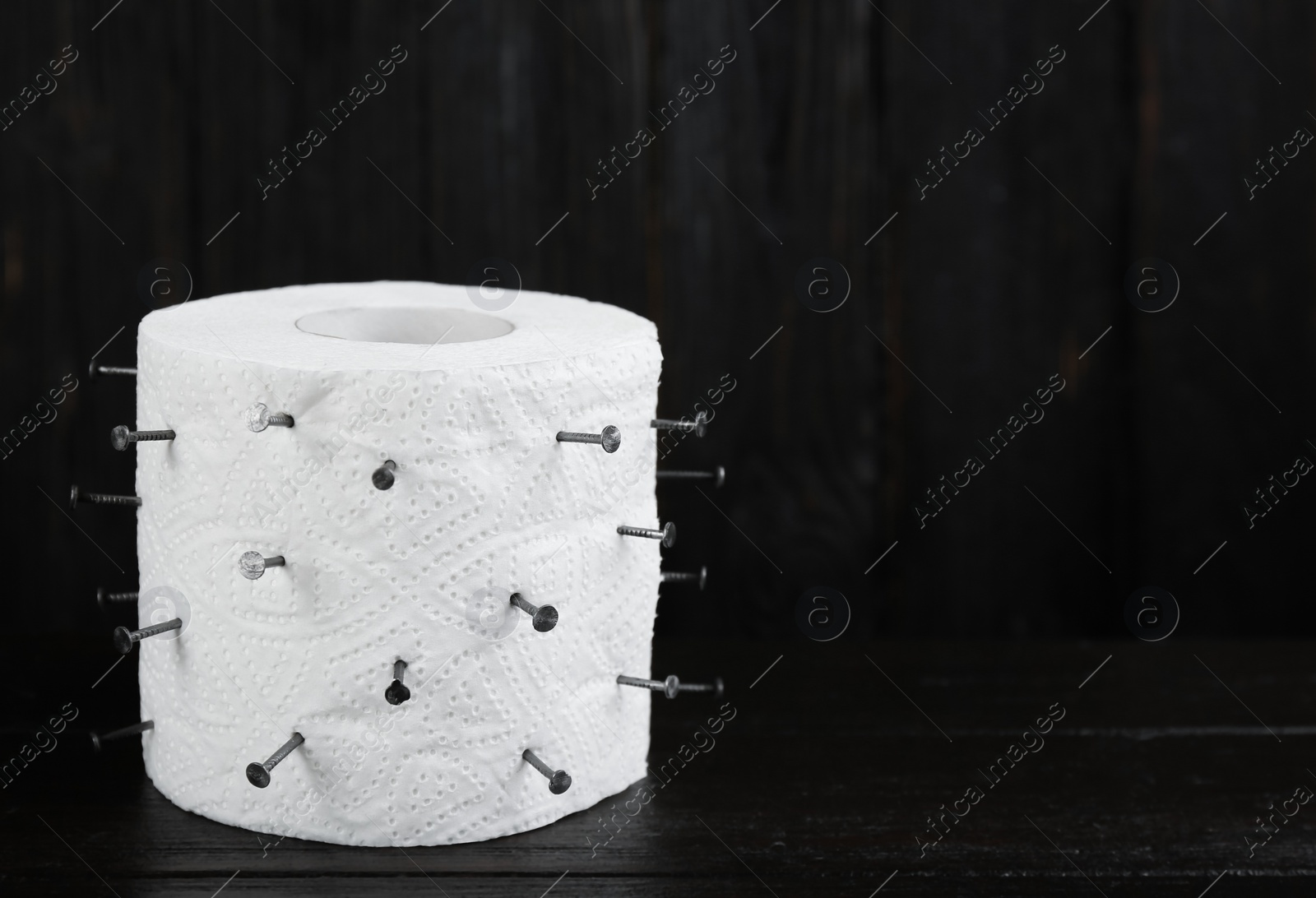 Photo of Roll of toilet paper with nails on black wooden table, space for text. Hemorrhoid problems