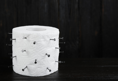 Photo of Roll of toilet paper with nails on black wooden table, space for text. Hemorrhoid problems