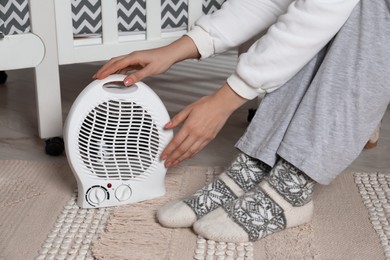 Photo of Young woman holding modern electric fan heater in child room, closeup