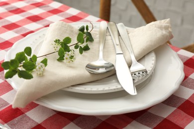 Stylish setting with cutlery, plates, napkin and floral decor on table, closeup