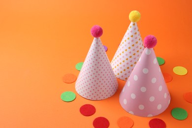 Party hats and colorful confetti on orange background. Space for text