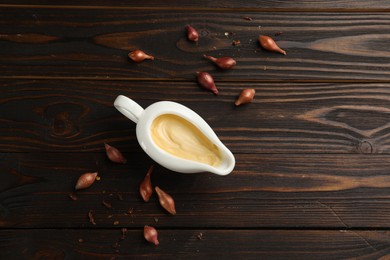 Tasty sauce in gravy boat, small onion bulbs and spice on wooden table, flat lay. Space for text