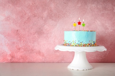 Fresh delicious birthday cake with candles on stand against color background. Space for text