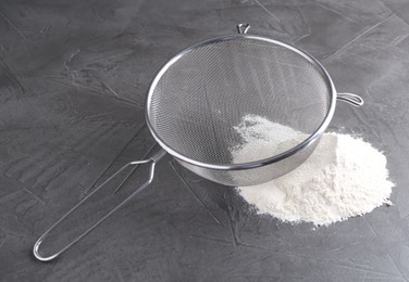 Photo of Metal sieve and flour on grey table