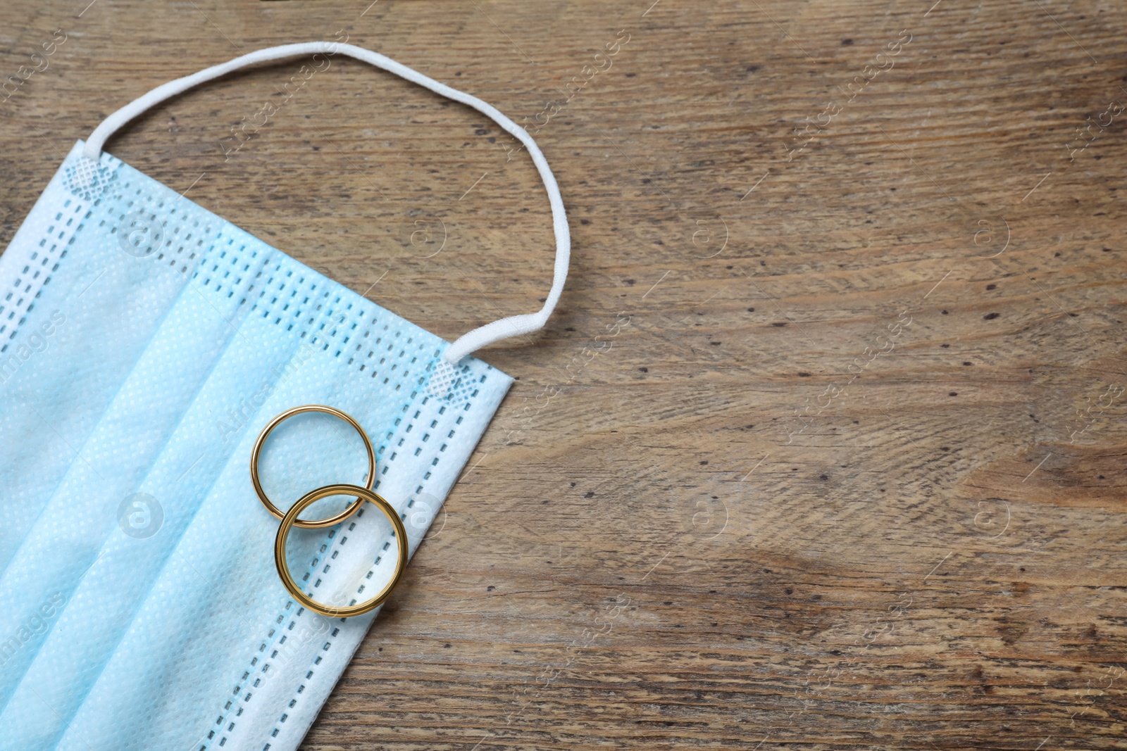 Photo of Protective mask and wedding rings on wooden table, flat lay with space for text. Divorce during coronavirus quarantine