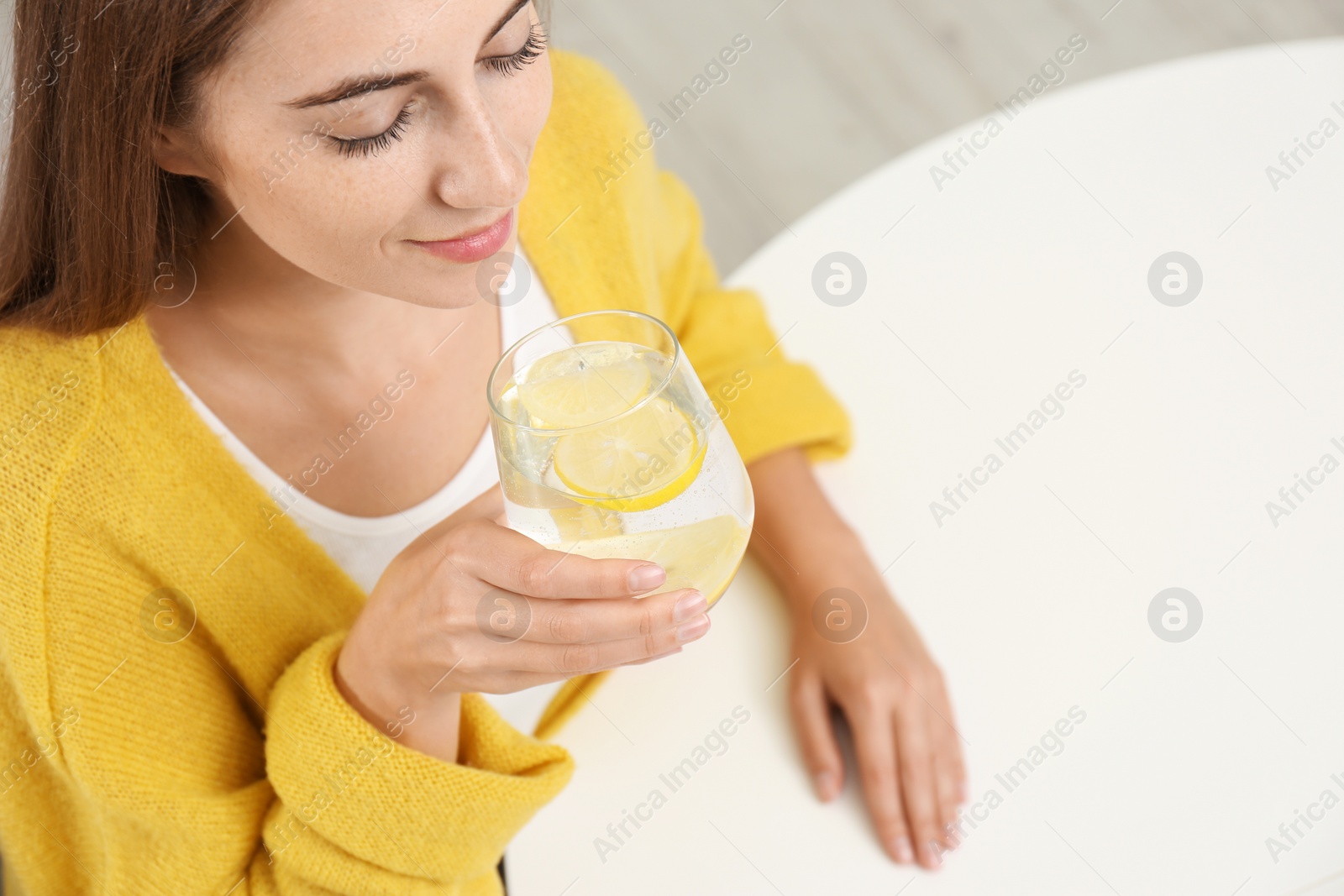 Photo of Young woman drinking lemon water at white table, above view