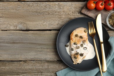 Photo of Delicious chicken fillet with capers and sauce served on wooden table, flat lay. Space for text