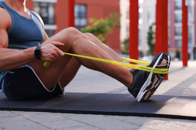 Photo of Muscular man doing exercise with elastic resistance band on mat at sports ground, closeup