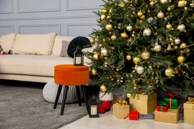 Photo of Gift boxes under Christmas tree, ottomans and sofa in living room