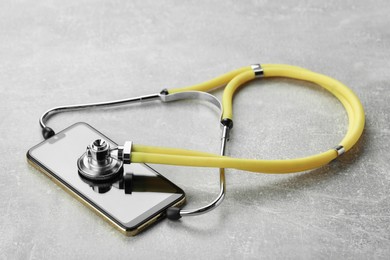 Stethoscope and modern smartphone on grey table