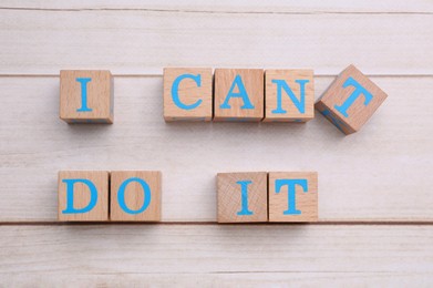 Photo of Motivation concept. Changing phrase from I Can't Do It into I Can Do It by removing cube with letter T on light wooden table, flat lay
