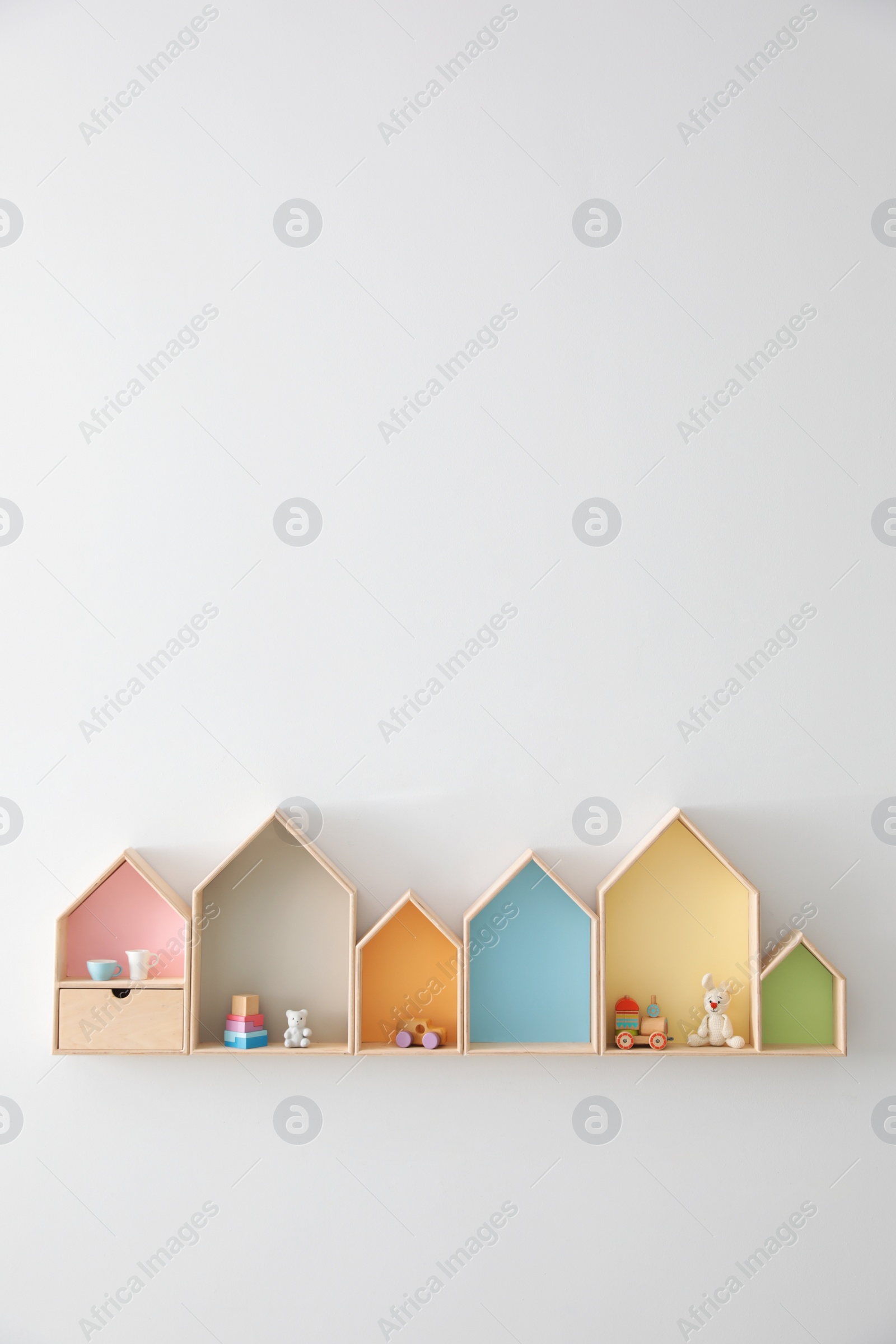 Photo of Different house shaped shelves with toys on white wall, space for text. Interior design