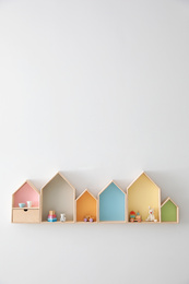 Different house shaped shelves with toys on white wall, space for text. Interior design