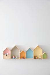 Photo of Different house shaped shelves with toys on white wall, space for text. Interior design