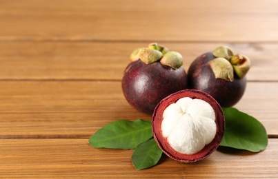 Photo of Fresh ripe mangosteen fruits on wooden table. Space for text