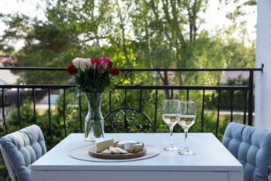Beautiful roses, glasses of wine and snacks on white table at balcony