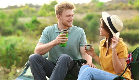 Photo of Young couple with hot drinks resting outdoors. Camping vacation