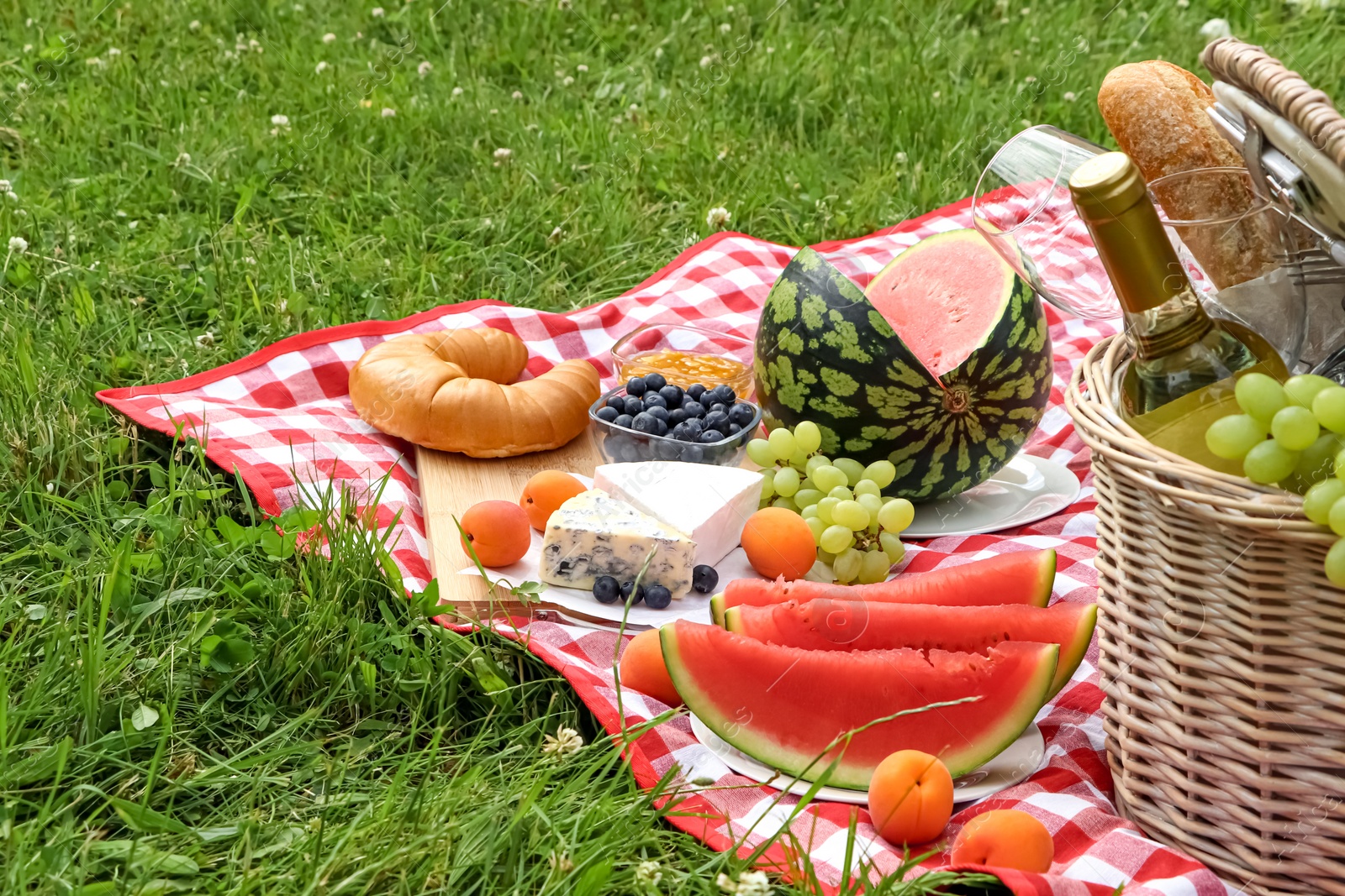 Photo of Picnic blanket with delicious food and wine outdoors on summer day