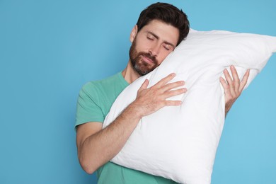 Photo of Sleepy handsome man hugging soft pillow on light blue background