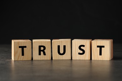 Photo of Word TRUST made with wooden cubes on grey table against black background