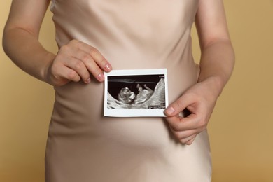Photo of Pregnant woman with ultrasound picture of baby on beige background, closeup