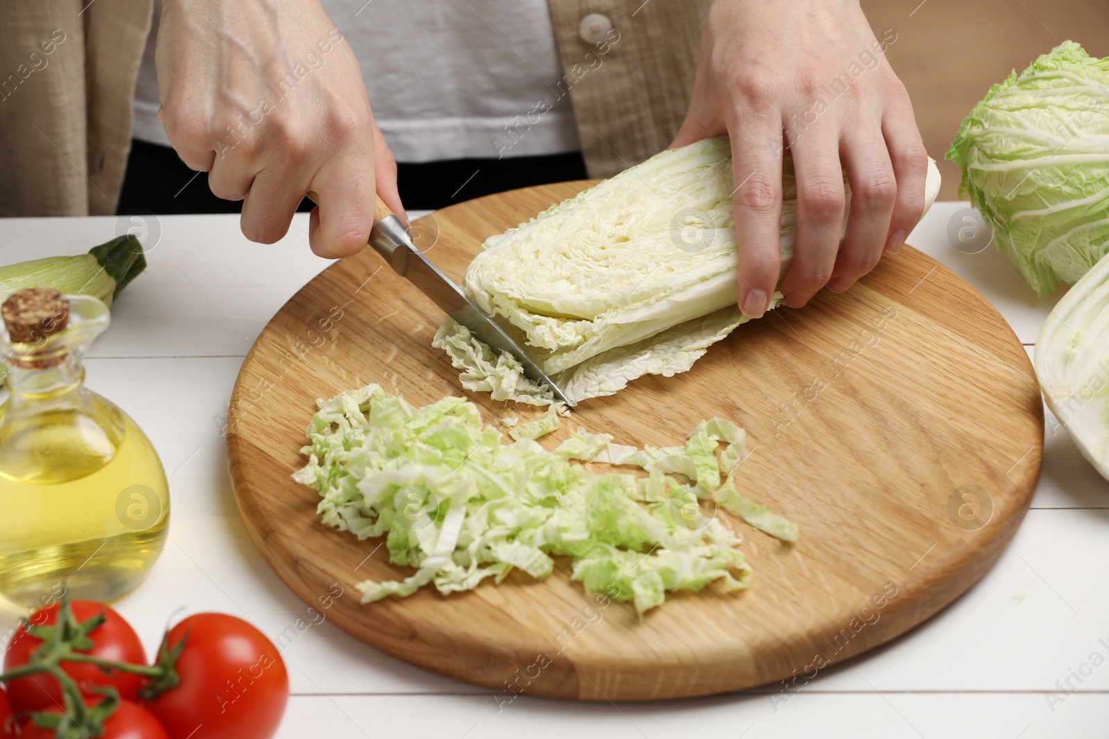 Photo of Woman cutting fresh chinese cabbage at white wooden table, closeup