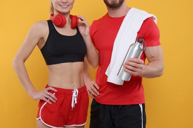 Photo of Athletic people with headphones, thermo bottle and towel on yellow background, closeup
