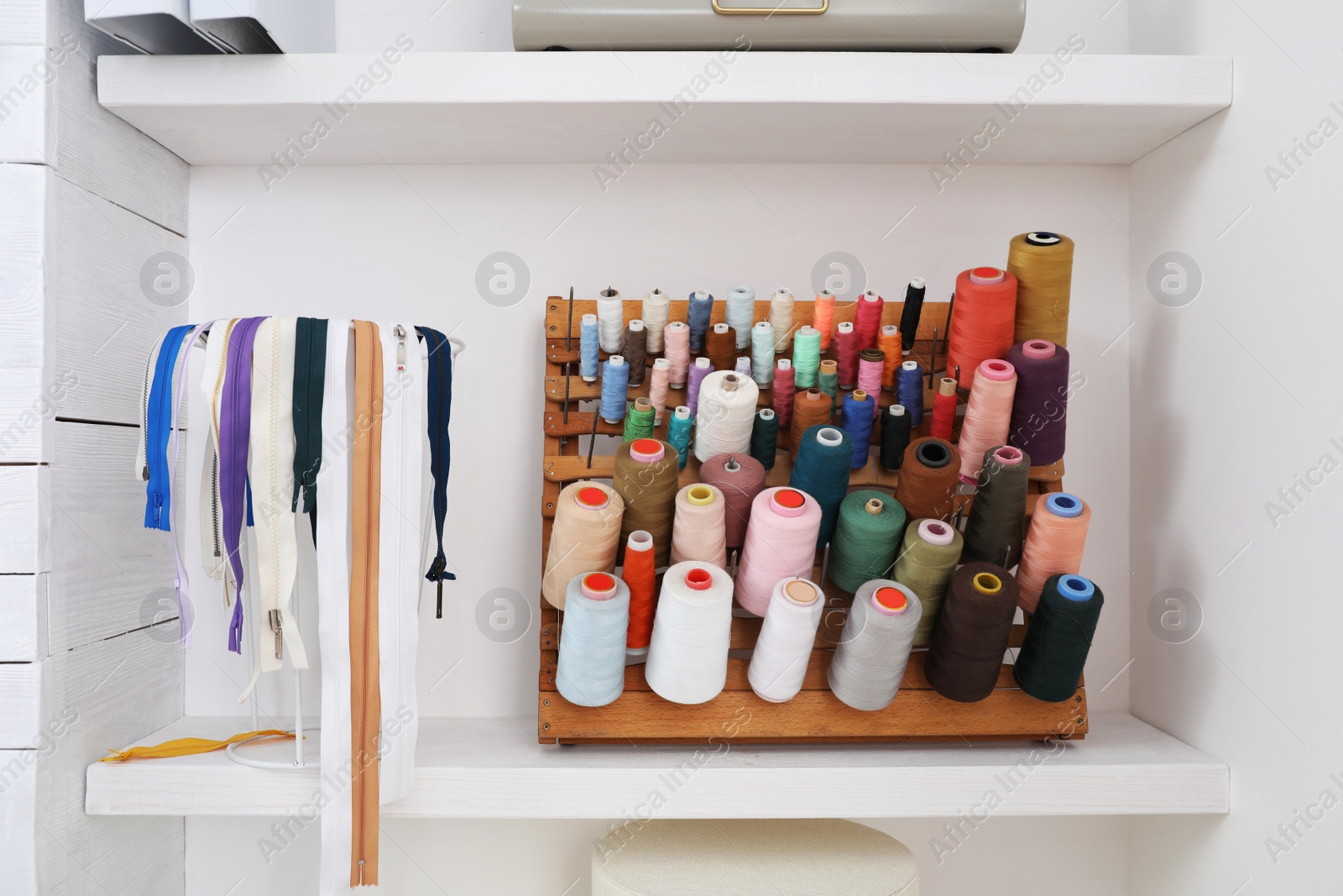 Photo of Wooden holder with collection of different threads on shelf in tailor studio