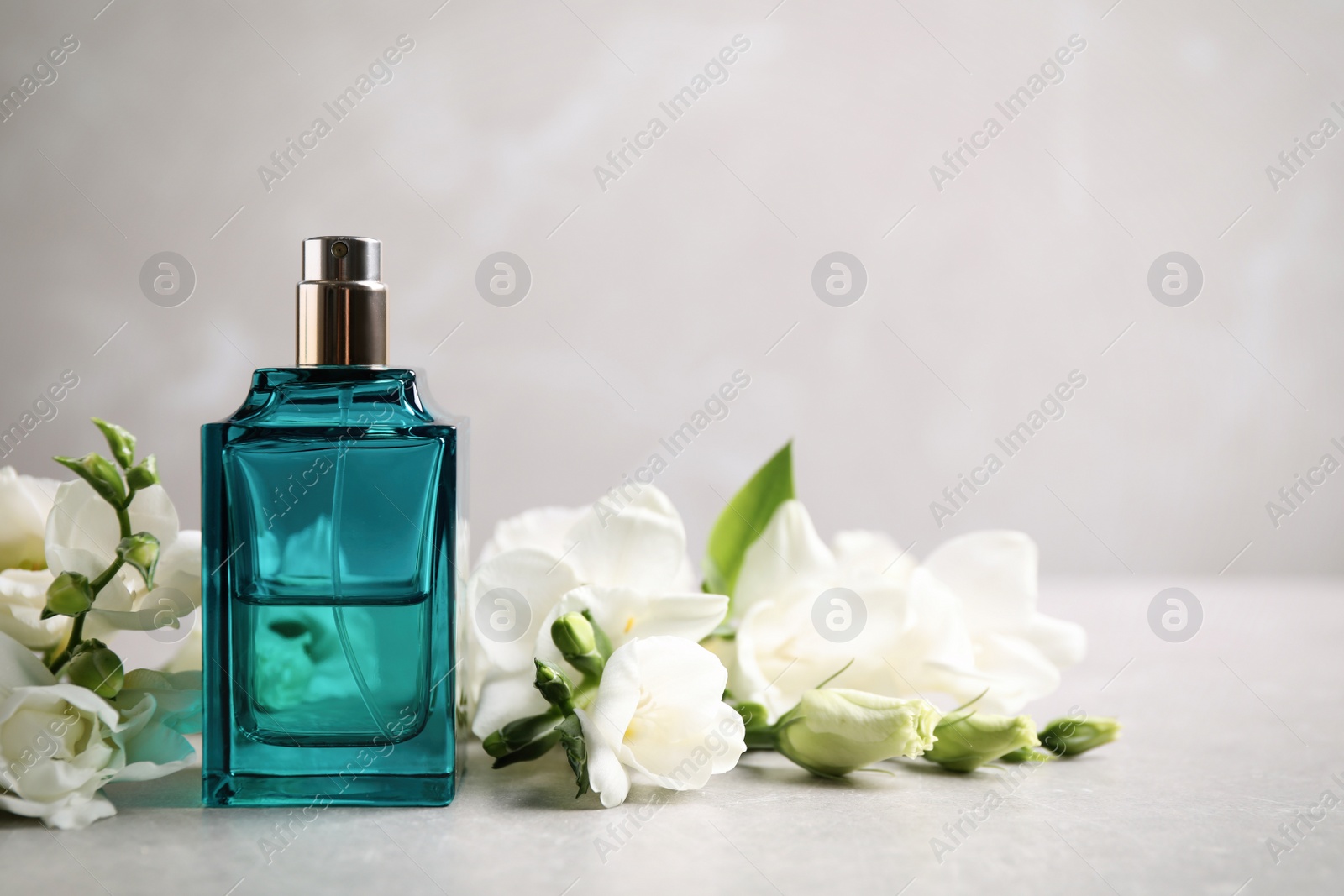 Photo of Bottle of perfume and beautiful flowers on light table. Space for text